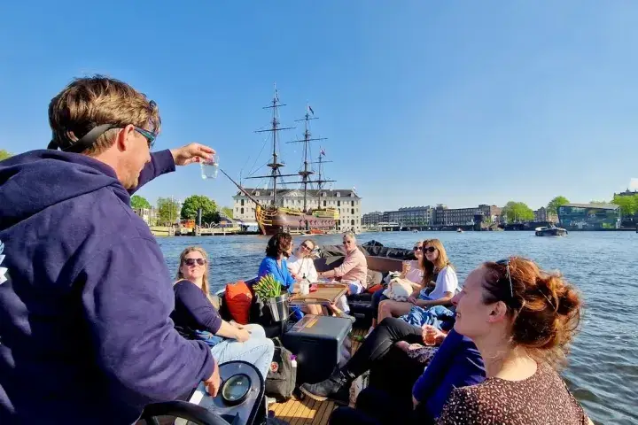 a group of people on an open boat tour looking at the tour guide holding a glass of canal water