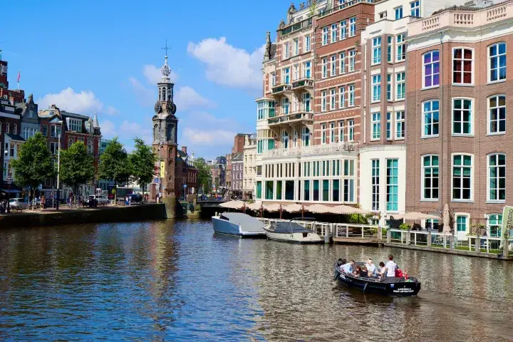 a cityscape of Amsterdam with a small open boat cruising the Amstel River