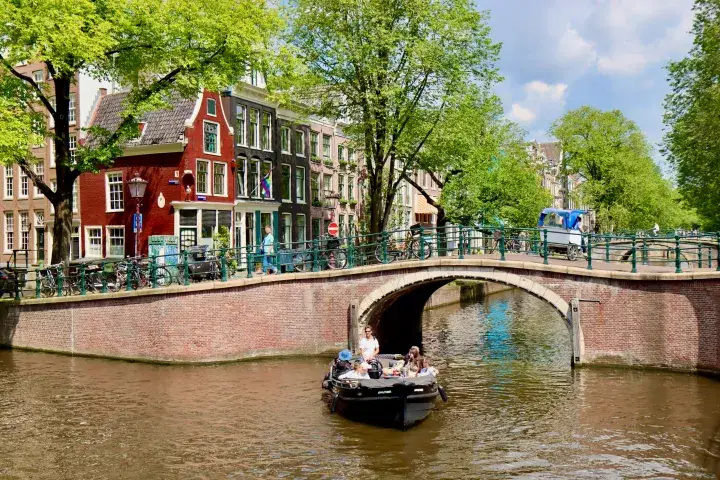 a small boat tour in front of a traditional Amsterdam canal bridge
