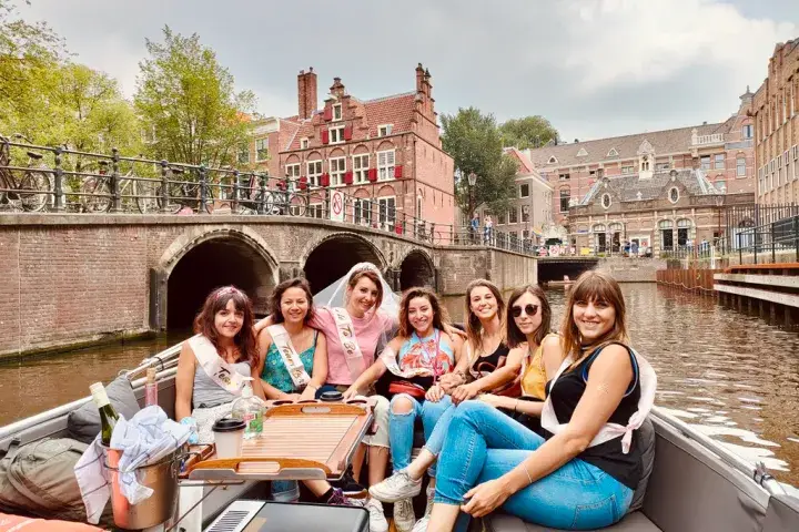 A group of Ladies and a bride to be sitting on an open boat in front of iconic Amsterdam Houses