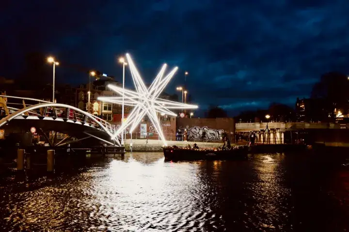 a small open boat cruising towards big light art in the shape of the Polar Star from the Amsterdam Light Festival