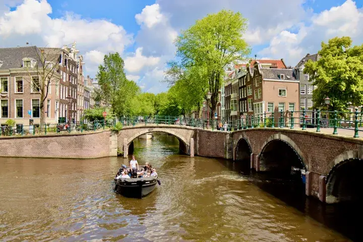 a small open boat on an Amsterdam canal crossing with bridges and canal houses in the background