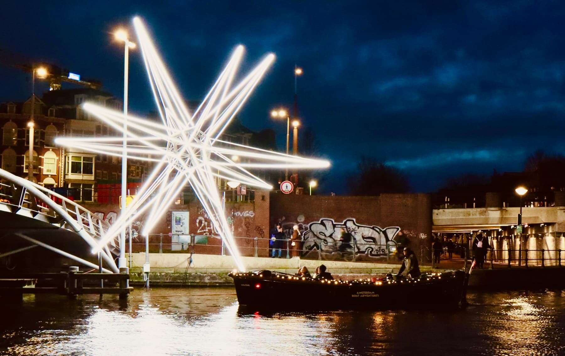 Illuminated street art and boats on the Amsterdam canal at night during an Amsterdam light festival boat tour.