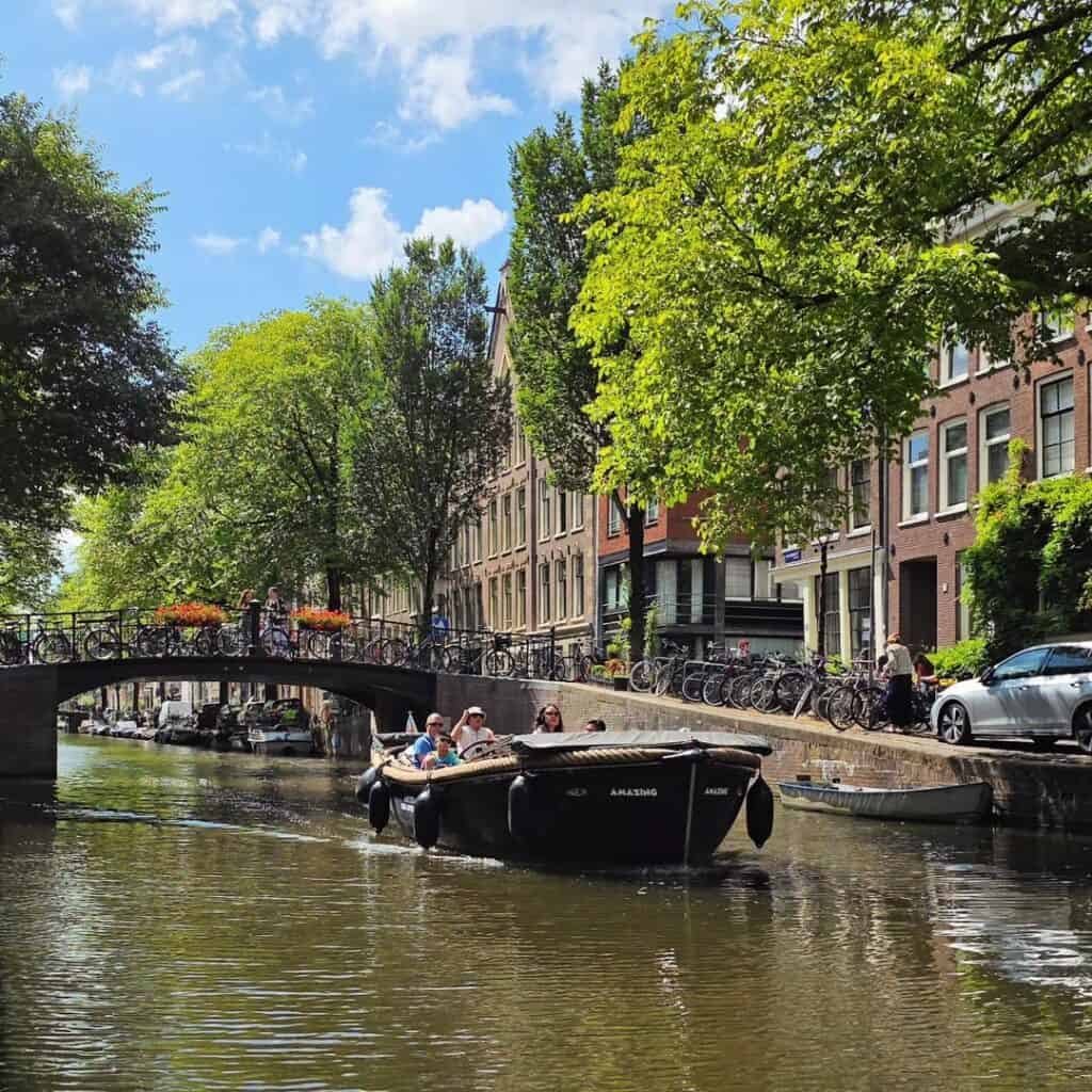 a small open boat cruising through an Amsterdam Canal in the Jordaan district