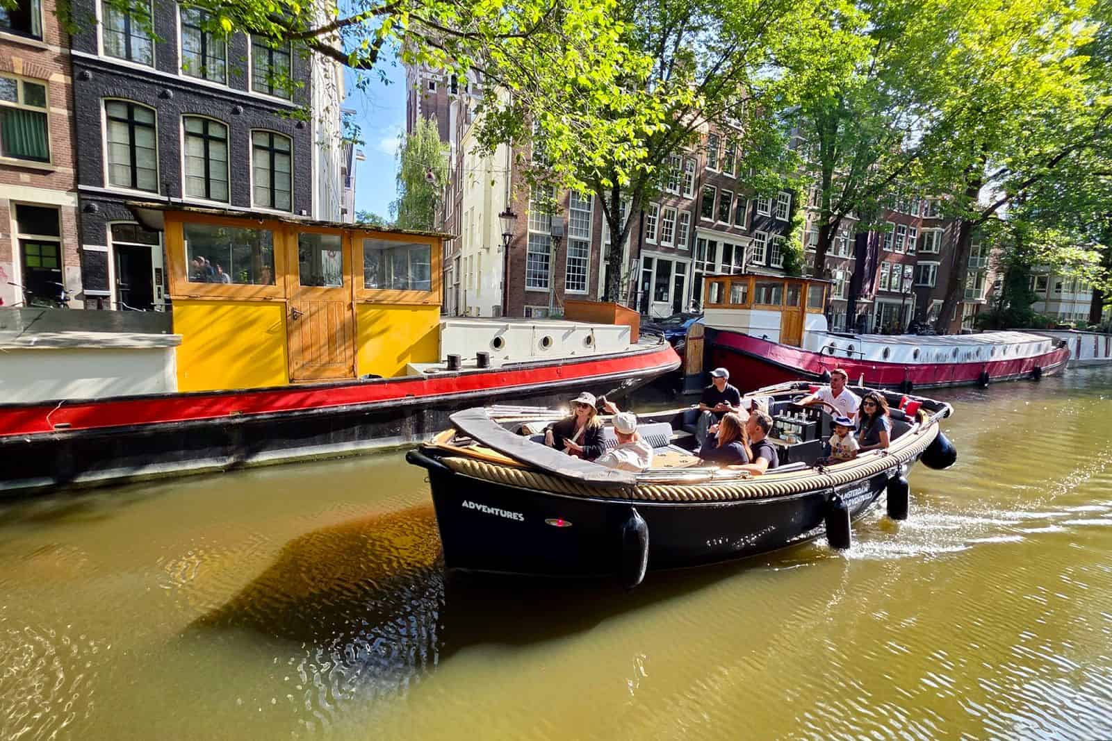 An open boat with tourist on board cruising down a small Amsterdam canal