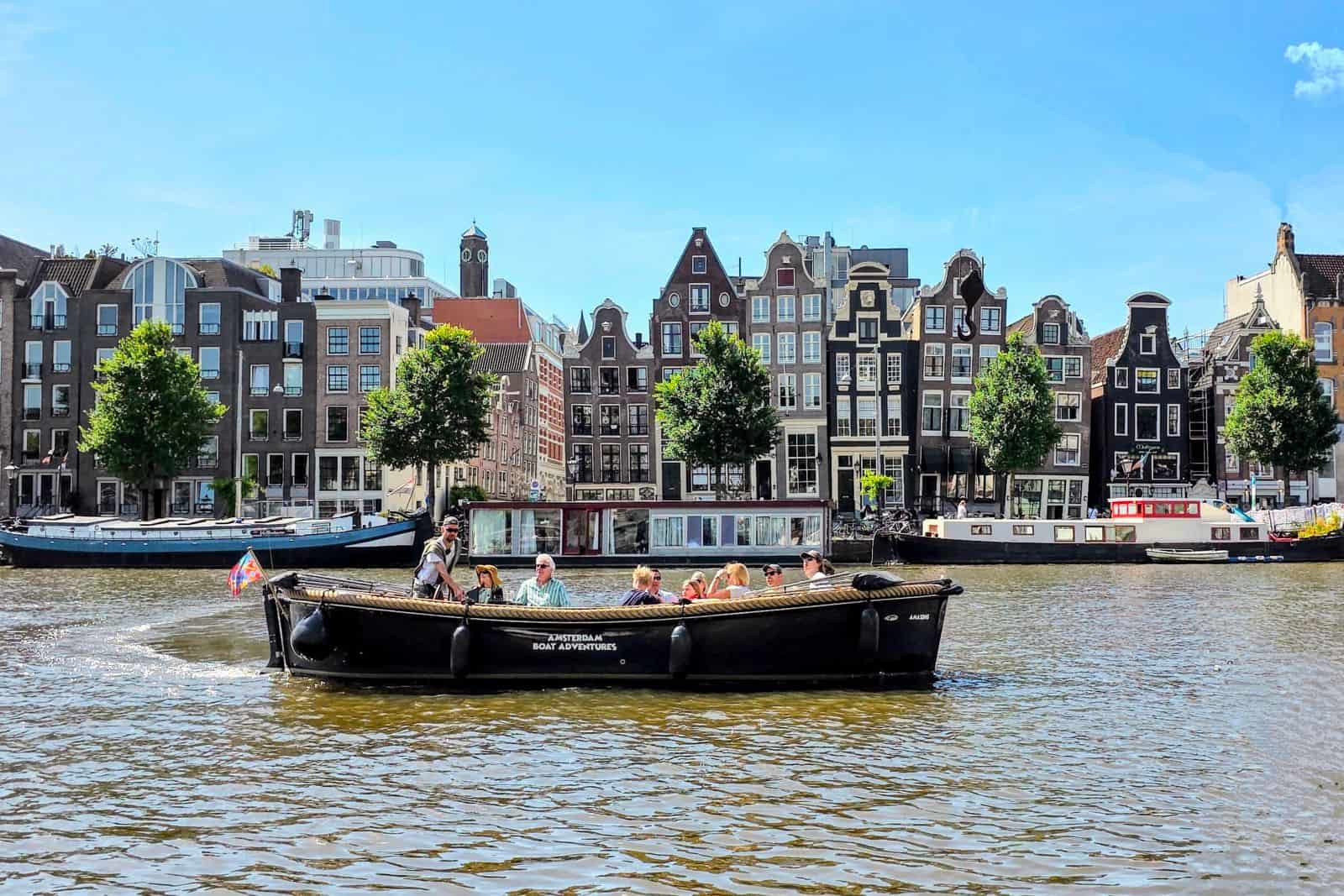 an open boat with tourist on the Amstel river in front of the dancing houses