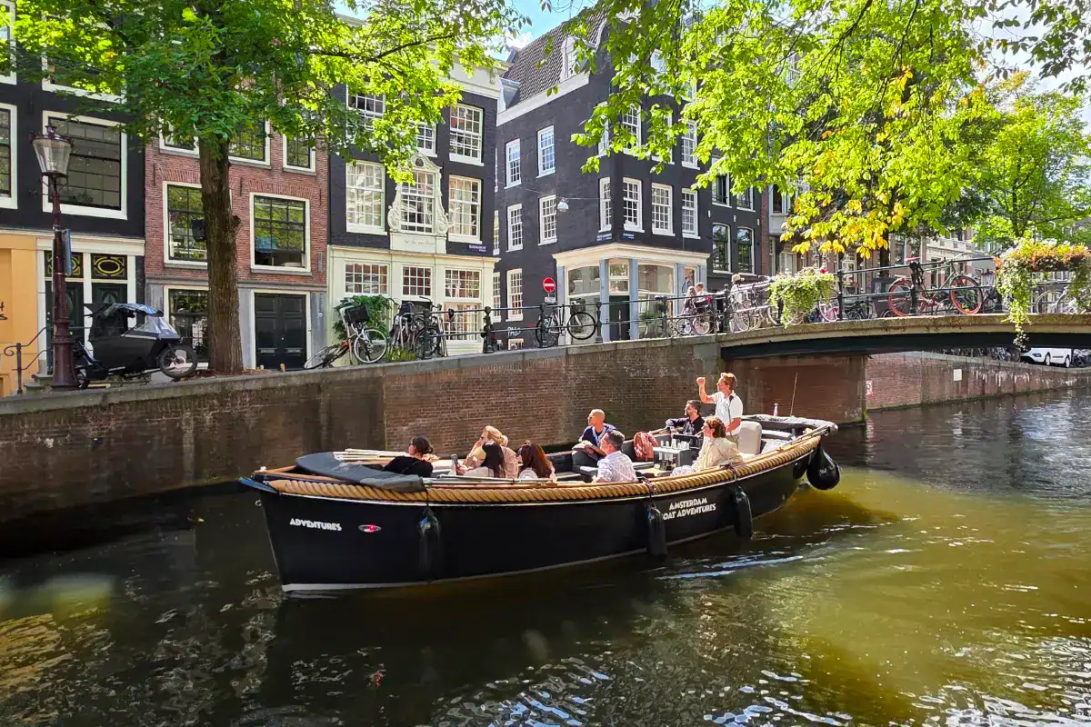 Bicycle-lined canal street with classic Dutch buildings and a boat tour in Amsterdam.