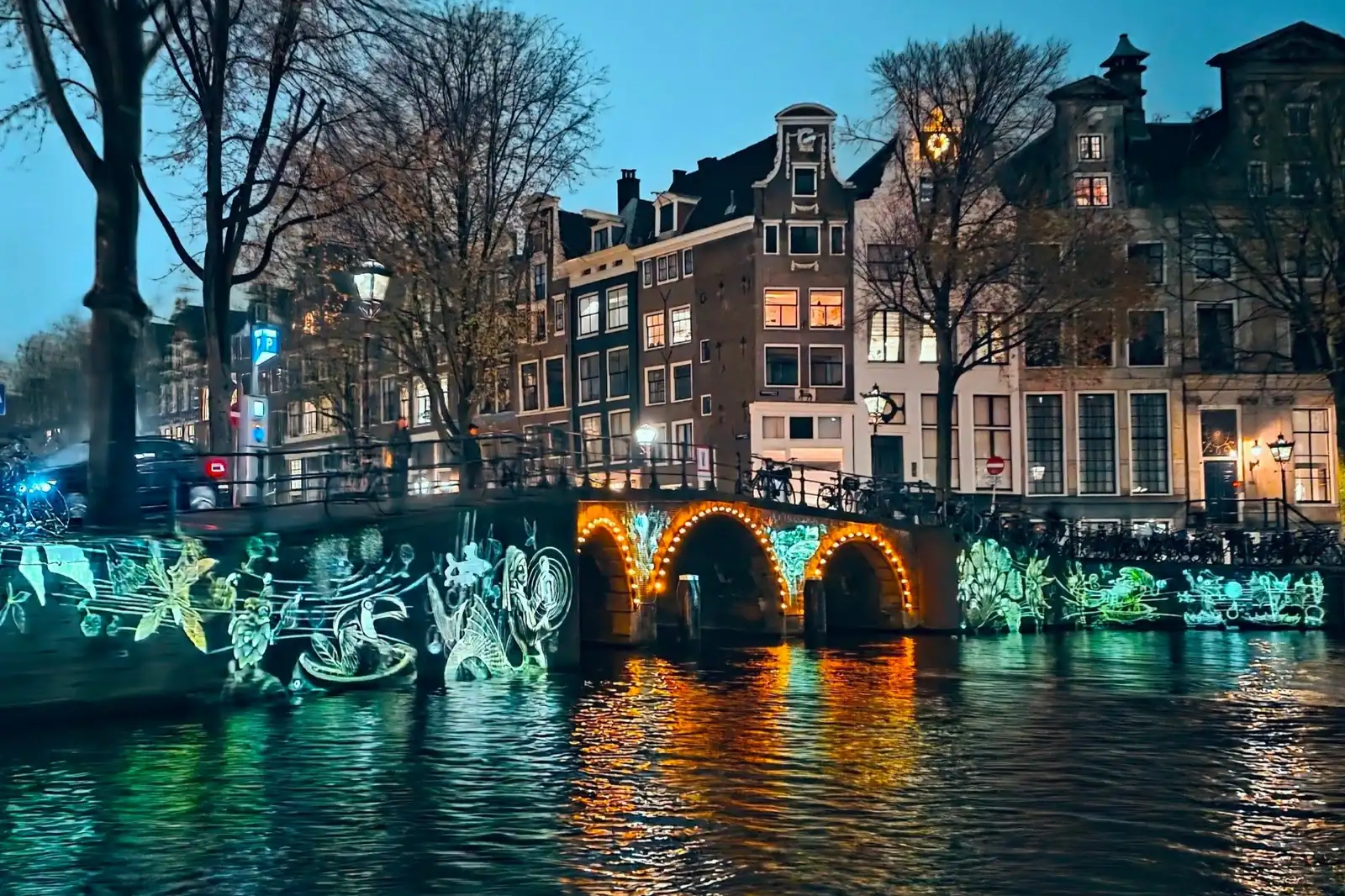 Beautiful illuminated canal during night in Amsterdam showing houses and bridge.