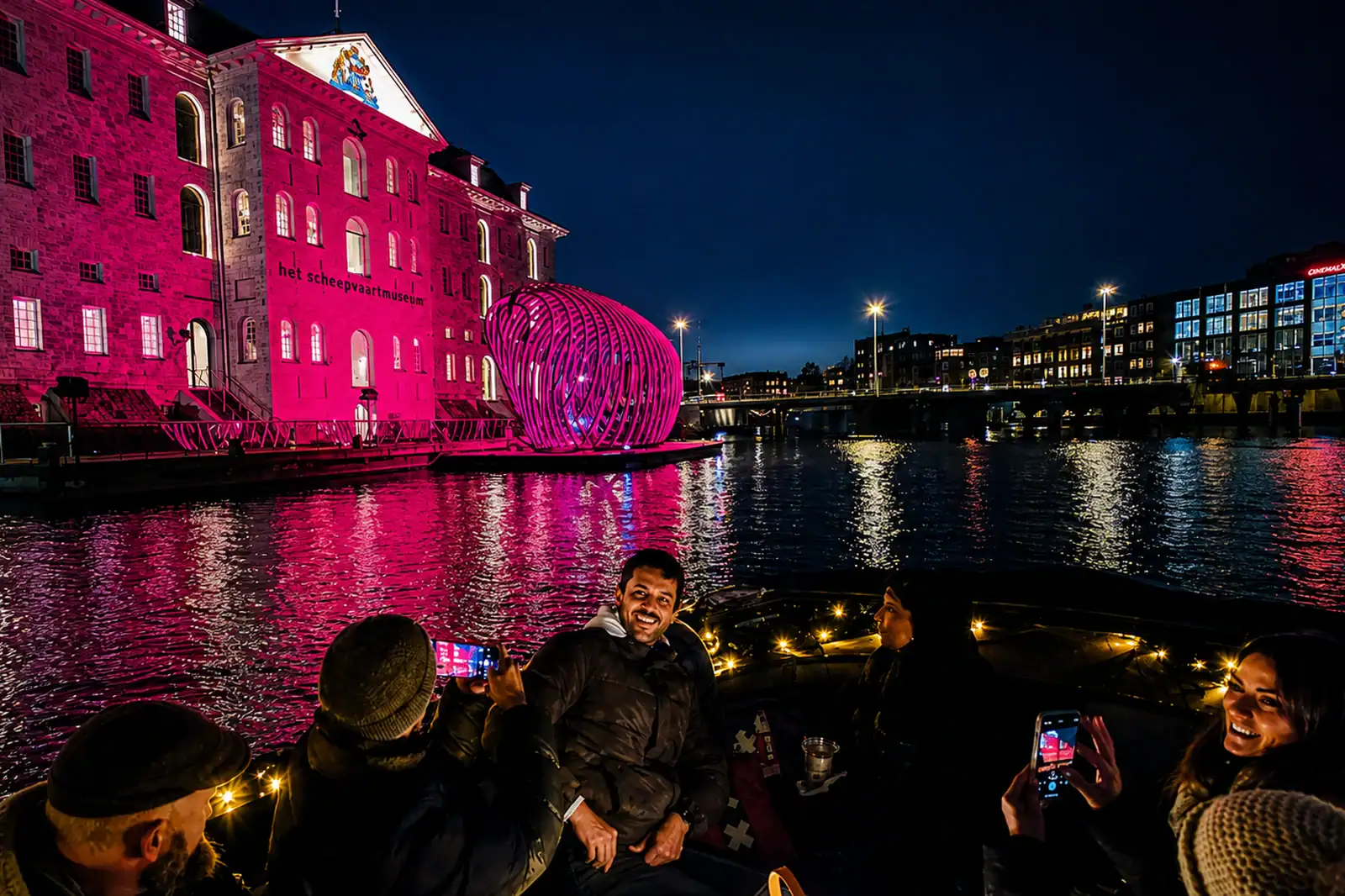 a group of people sitting on an open boat while seeing light art from Amsterdam Light Festival