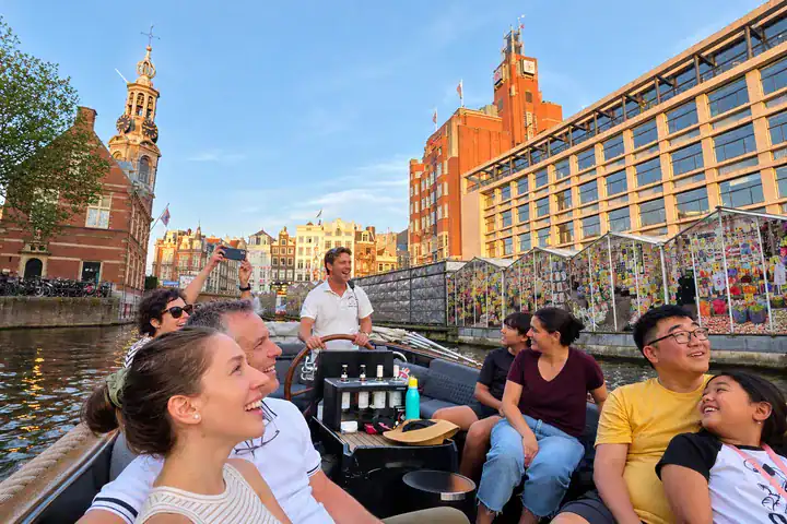 Guests enjoying an Amsterdam evening boat tour past the Floating Flower Market and Munt Tower.