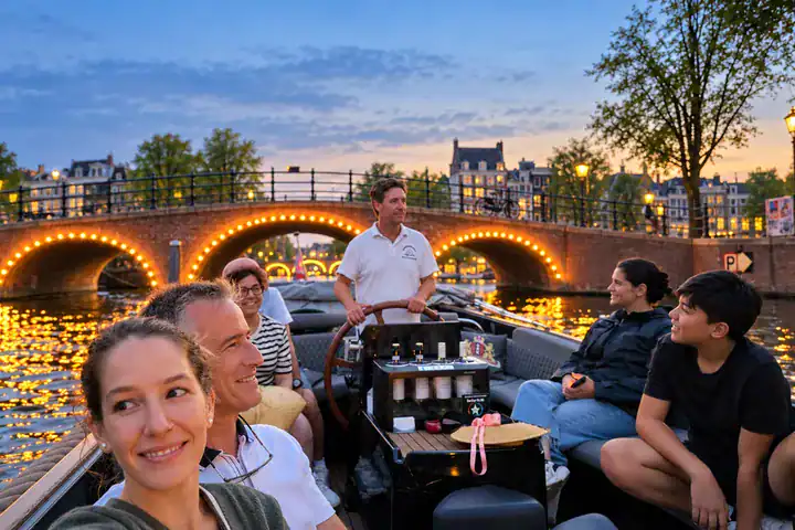 Small-group evening boat tour in Amsterdam with guests cruising past illuminated canal bridges.